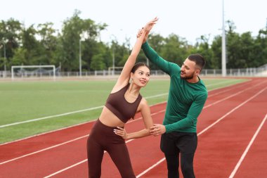 Stadyumda esneme hareketleri yapan Asyalı spor eğitmeni bir kadın.