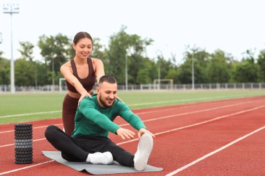 Stadyumda esneme hareketleri yapan antrenörü olan sporcu bir adam.