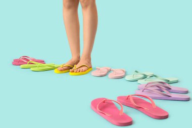 Mavi arka planda renkli parmak arası terlikleri olan kadın bacakları