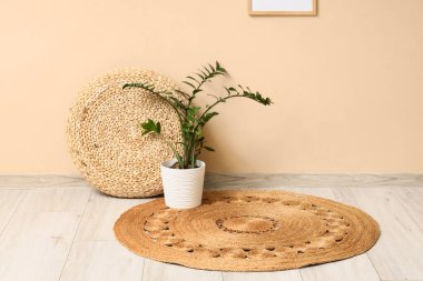 Odadaki bej duvarın yakınındaki hasır halıda bitkili Rattan puf.
