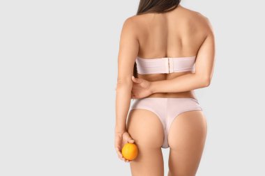 Selülit sorunu olan iç çamaşırlı genç bir kadın ve arka planda turuncu bir kadın.