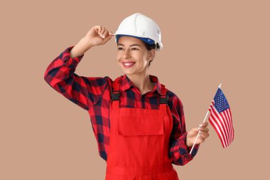 Bej arka planda Amerikan bayrağı olan kasklı bir kadın işçi. İşçi Bayramı kutlamaları