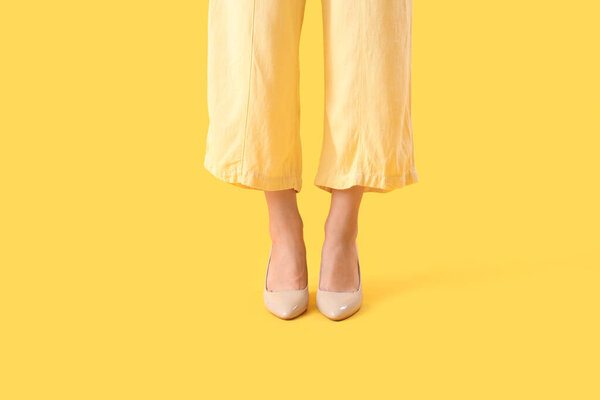 Ноги молодой женщины на стильных бежевых каблуках на жёлтом фоне