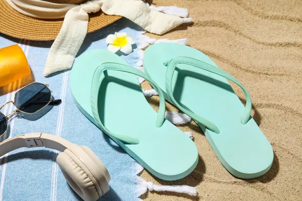 Plaj ayakkabıları, kulaklıkları ve kumsaldaki aksesuarları arka plan olarak, yakın plan.