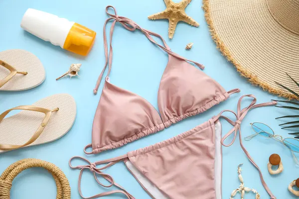 Şık bir mayo, güneş kremi şişesi ve mavi arka planda plaj aksesuarları, yakın plan.