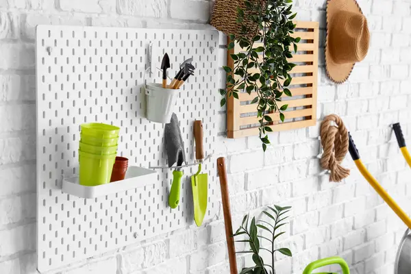 Atölyedeki beyaz tuğla duvarda bahçe aletleri olan tahta.