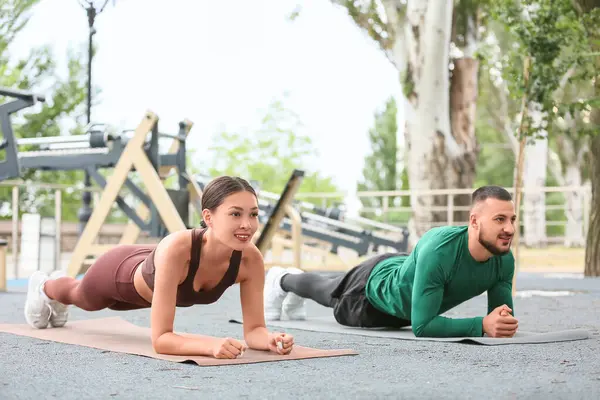Kişisel antrenörü olan genç bir Asyalı kadın spor sahasında kalas yapıyor.