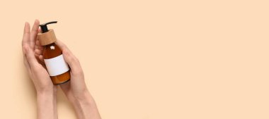 Kadın elleri bej arka planda kozmetik ürünü şişesini tutuyor ve metin için yer var.