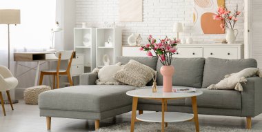 Güzel manolya çiçekleri ve dergilerle dolu vazo modern oturma odasındaki gri kanepenin yanında.