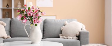 Üzerinde güzel manolya çiçekleri olan vazo şık oturma odasındaki gri kanepenin yanında.