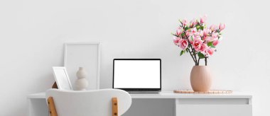 Işık duvarının yanındaki masanın üzerinde manolya çiçekleri olan vazo.