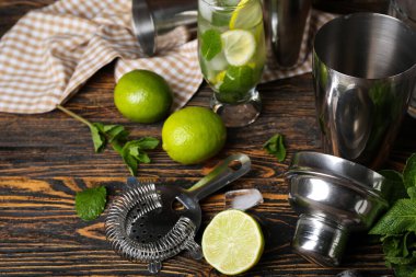 Çalkalayıcı, süzgeç ve ahşap arka planda mojito hazırlamak için malzemeler.