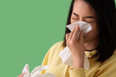 Yeşil arka planda mendilleri olan Asyalı hasta kadın, yakın plan.