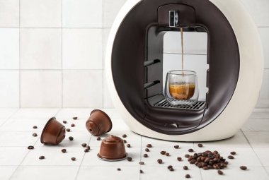 Damlayan espresso, fincan, kapsül kahve makinesi ve beyaz masa üzerinde fasulye.