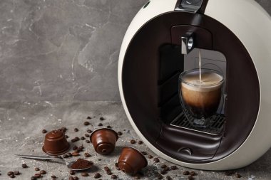 Damlayan espresso, fincan, kapsül kahve makinesi ve gri grunge masasında fasulye.