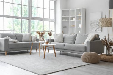 Işıl ışıl oturma odasının içi. Büyük pencerenin yanında rahat gri koltuklar ve kahve masası.