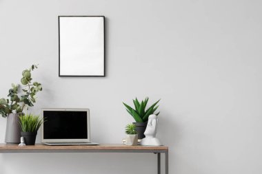 Modern dizüstü bilgisayar ve beyaz duvarın yanındaki masada farklı ev bitkileri.