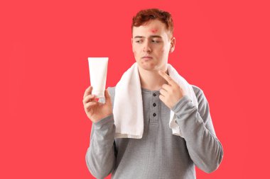 Kırmızı arka planda sivilce ilacı olan genç bir çocuk.