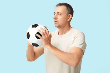 Yakışıklı olgun bir adam mavi arka planda futbol topuyla oynuyor.