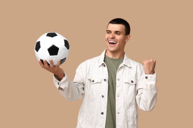 Kahverengi arka planda futbol topu olan yakışıklı genç adam.