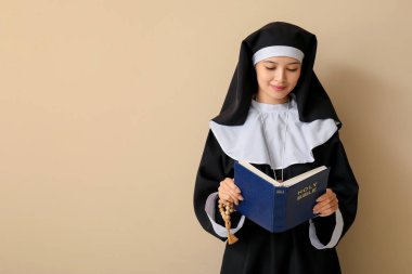 Bej arkaplanda İncil okuyan güzel Asyalı genç bir rahibe.
