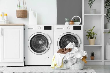 Çamaşır odasında çamaşır makinelerinin yanında kirli çamaşırlarla dolu bir sepet.