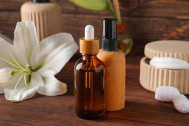 Ahşap arka planda kozmetik ürünleri, pamuk pedler ve zambak çiçekleri.