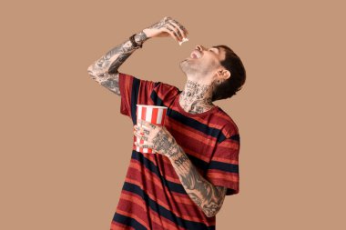 Kahverengi arka planda patlamış mısır kovası olan mutlu genç adam.