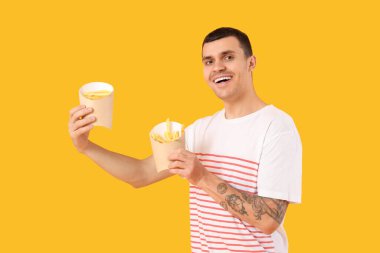 Sarı arka planda patates kızartması olan mutlu genç adam.