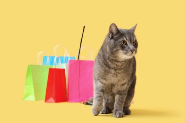 Sarı arka planda sevimli kedi ve alışveriş torbaları.