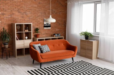 Turuncu kanepesi, lambası ve raf ünitesi olan bir çatı katı tarzı oturma odası.