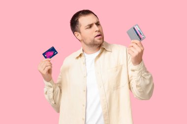 Pembe arka planda kredi kartı ve cüzdanı olan genç bir adam.
