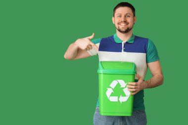 Yeşil arka planda geri dönüşüm logosu olan çöp kutusunu gösteren mutlu genç adam. Ekoloji kavramı