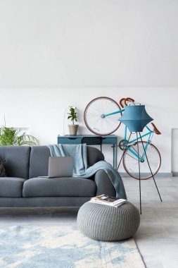 Siyah kanepesi, dizüstü bilgisayarı ve bisikleti olan beyaz bir oturma odası.