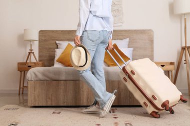 Otel odasında bavulu ve şapkası olan bir kadın.