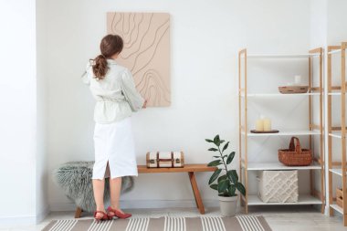 Güzel odadaki beyaz duvara resim asan güzel bir kadın.