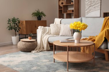 Interior of stylish living room with grey sofa, plaid, coffee table and flowers