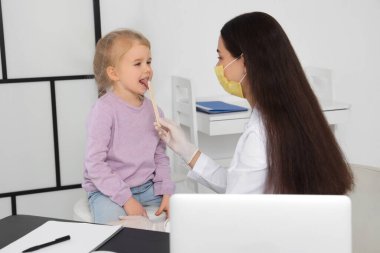Klinikteki masada küçük bir kızın boğazını dil bastırıcı ile muayene eden kadın bir çocuk doktoru.