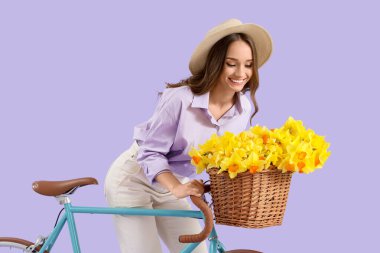 Leylak arka planında nergis ve bisikleti olan güzel genç bir kadın.