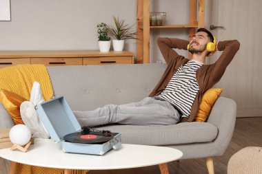 Evde müzik dinleyen kulaklıklı genç sakallı bir adam.