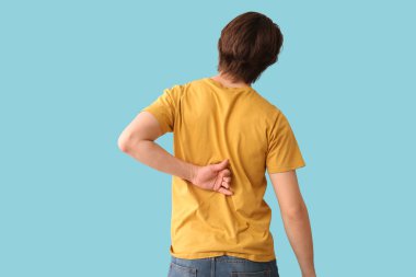 Mavi arka planda sırt ağrısı çeken yakışıklı genç adam.