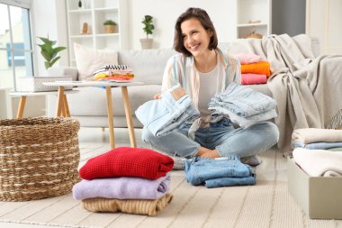 Genç bir kadın evde farklı giysiler katlıyor.