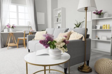 İçinde leylak çiçekleri ve dergi olan vazo oturma odasının iç tarafında.