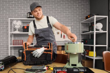 Atölyede kahve makinesini tamir eden bir çanta dolusu aletle çalışan bir erkek işçi.