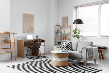 Gri kanepesi, sehpası, işyeri ve raf ünitesi olan şık bir oturma odası.