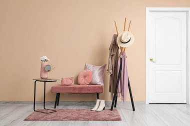 Samimi bir bank, elbise ve halı ile bej duvarın yanında.