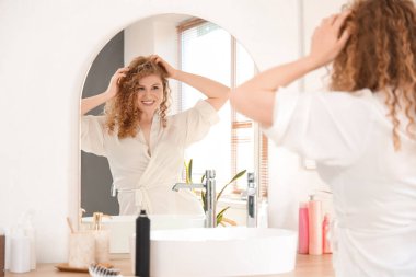 Genç bir kadın banyoda aynanın yanında kuru şampuan sürüyor.