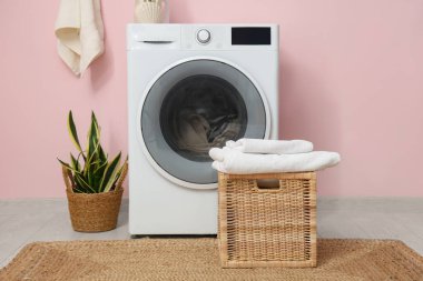 Çamaşırları, sepeti ve pembe duvarı olan modern çamaşır makinesi.