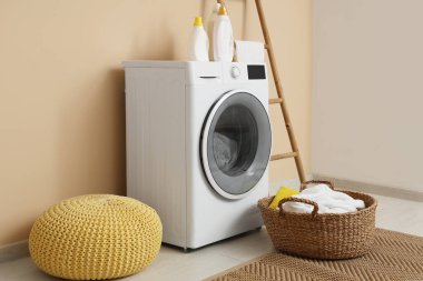Bej duvarın yanında merdiven, sepet ve puf ile modern çamaşır makinesi