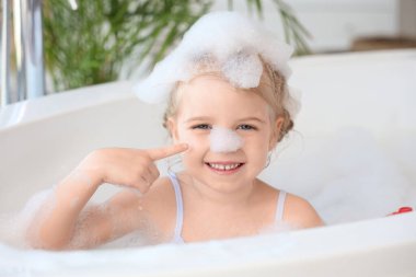 Küçük tatlı kız banyoda köpükle banyo yapıyor.